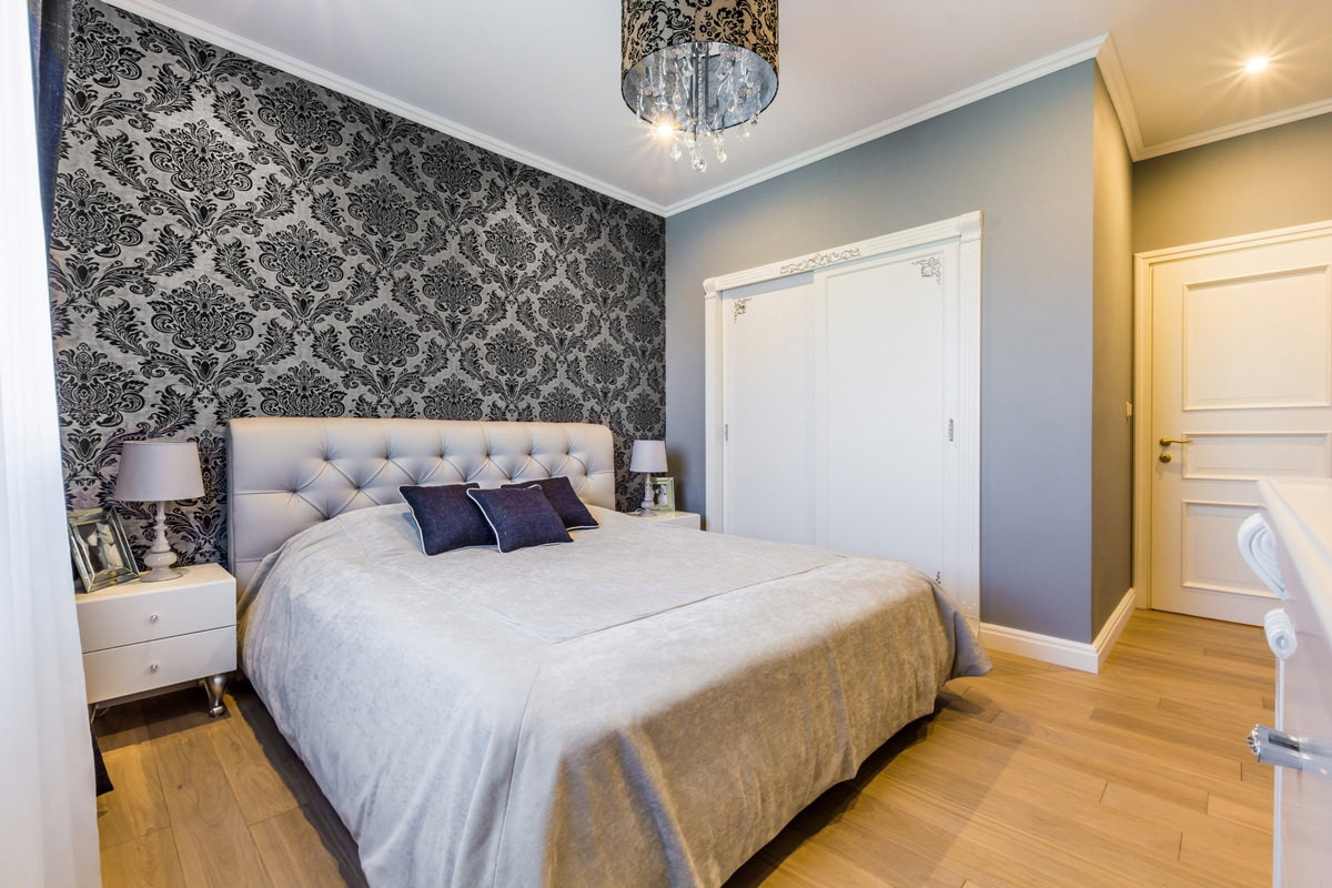 Gray wallpaper with a dark monogram pattern in the interior of the bedroom