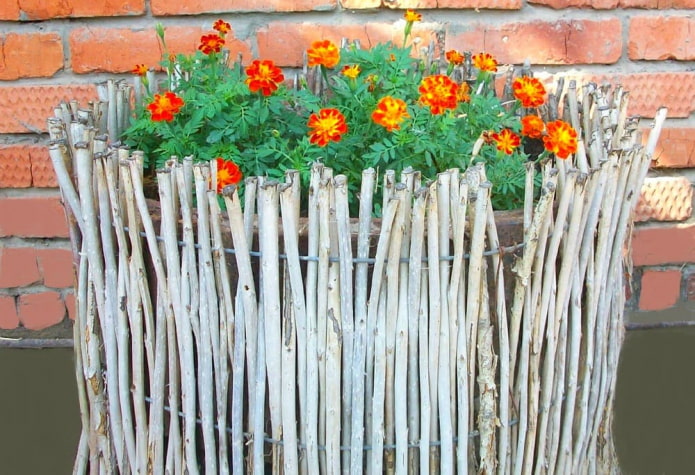 Dekoration der Seiten des Blumenbeets mit dünnen Zweigen, vertikal in den Drahtrahmen eingesetzt
