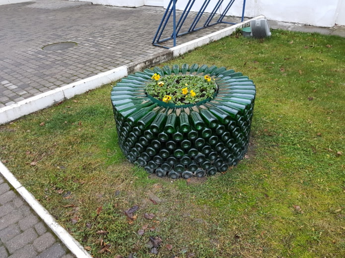 ein rundes Blumenbeet mit einem Rand aus übereinander gestapelten Glasflaschen