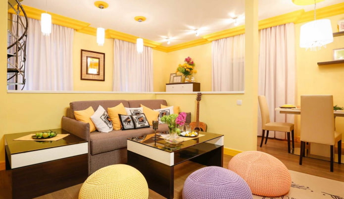 ห้องนั่งเล่นสีเหลืองอ่อนพร้อมหมอนหลากสีและออตโตมันถักไหมพรม